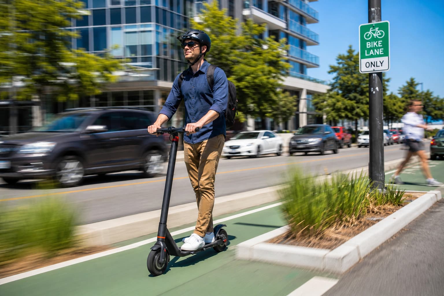 Une personne portant un casque de sécurité certifié roule en trottinette électrique sur une piste cyclable verte dédiée en ville, avec des voitures et piétons floutés en arrière-plan, sous un ciel bleu dégagé et ensoleillé.
